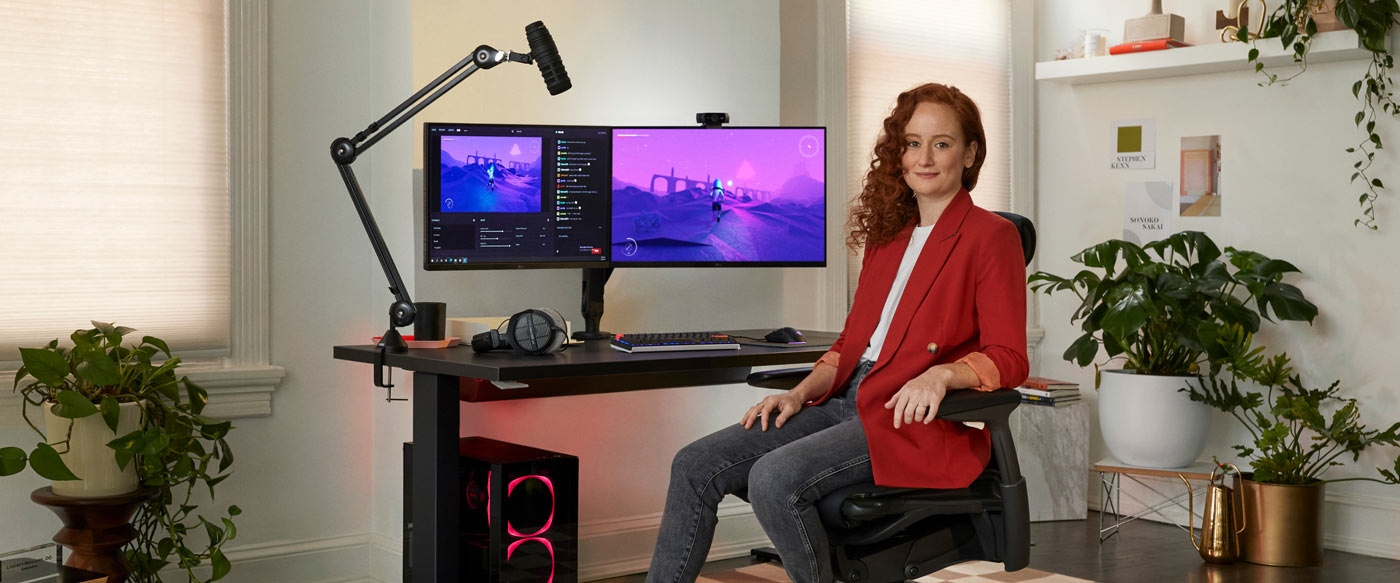 Photo du Dr Lindsey Migliore assis dans une chaise de jeu Embody face à la caméra, avec un bureau de jeu Nevi noir et des bras de support pour écran Ollin