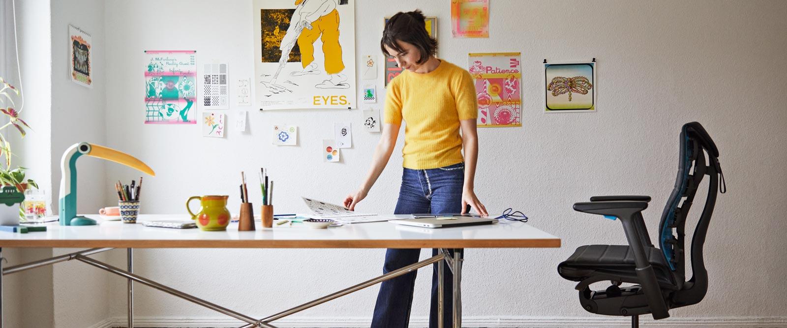 L'illustratrice, peintre et autrice Molly Rose Dyson debout dans son studio, devant son espace de travail, avec un fauteuil gaming Embody noir et bleu cyan