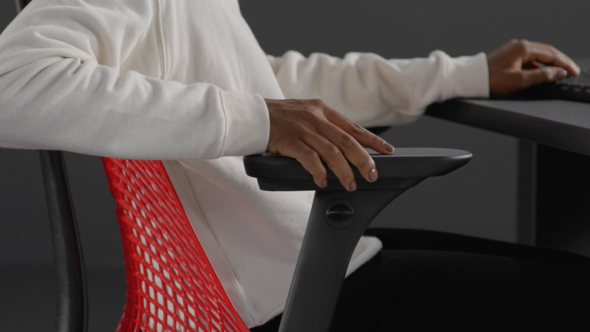 Vidéo d'une personne assise dans un fauteuil de jeu Sayl rouge et noir de Herman Miller, qui tend la main à côté du fauteuil pour en régler les accoudoirs.