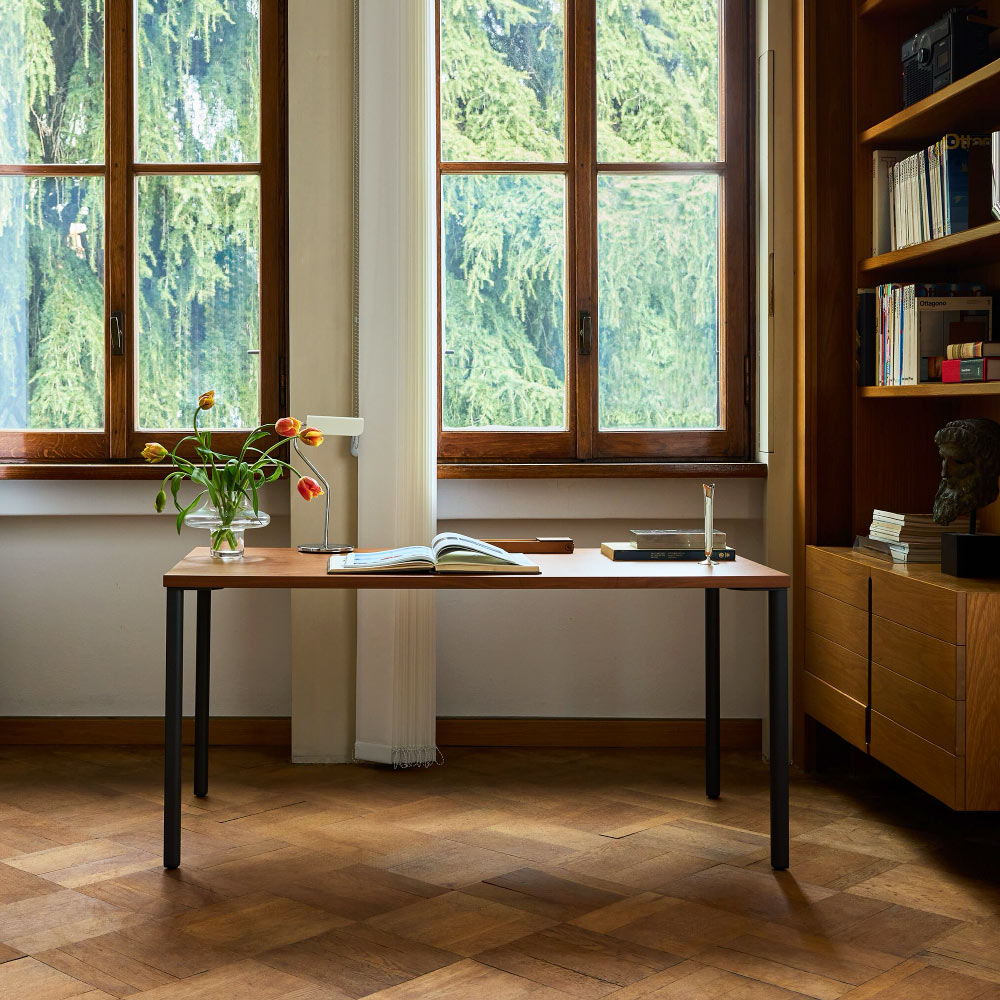 Un bureau Herman Miller OE1 avec un plateau en noyer et des pieds bleu marine. Avec une lampe HAY Apex de couleur crème.