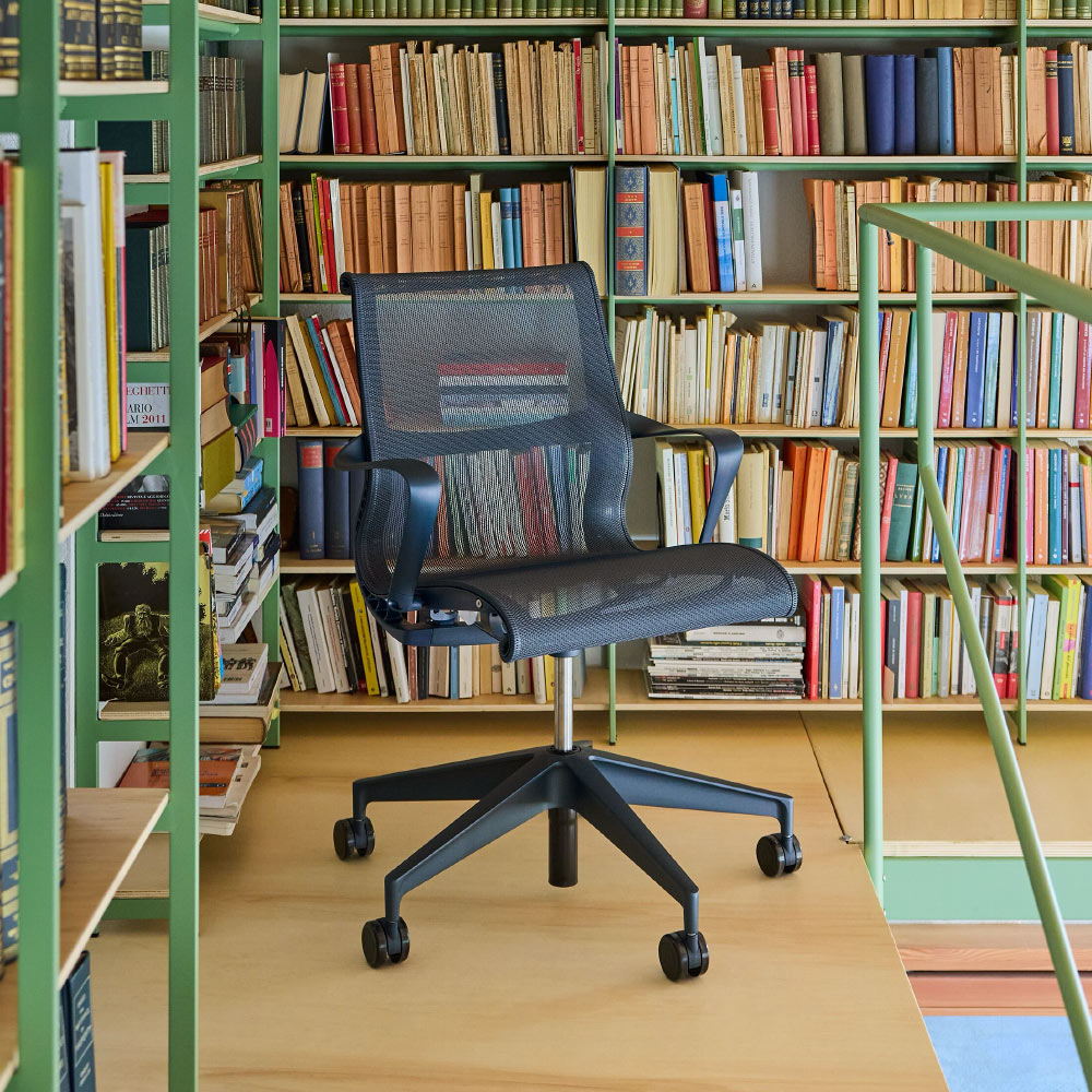 Un fauteuil de lecture ergonomique Setu d'Herman Miller, bleu marine, dans une bibliothèque d'intérieur colorée.