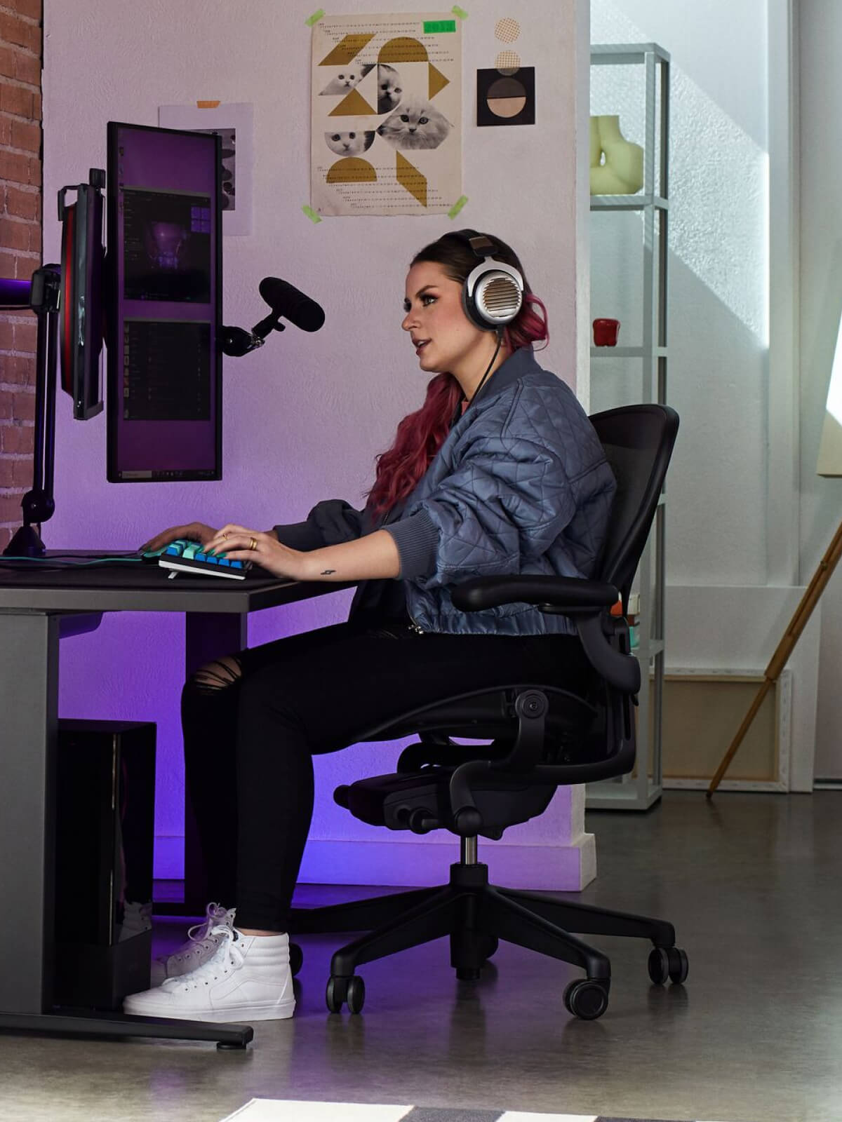 Electra jouant sur un fauteuil Aeron noir onyx avec un bureau gaming Nevi noir et un bras pour écran Ollin