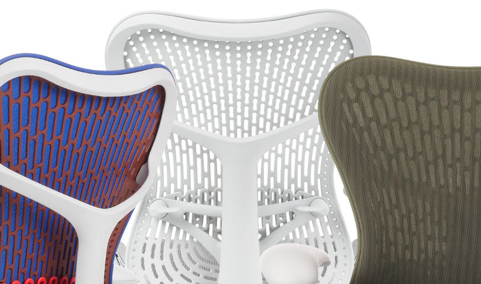 Gros plan sur trois chaises de bureau Mirra 2 d'Herman Miller, montrant la gamme de couleurs disponibles. La première est bleue, orange et blanche, la deuxième est uniquement blanche et la troisième est verte.