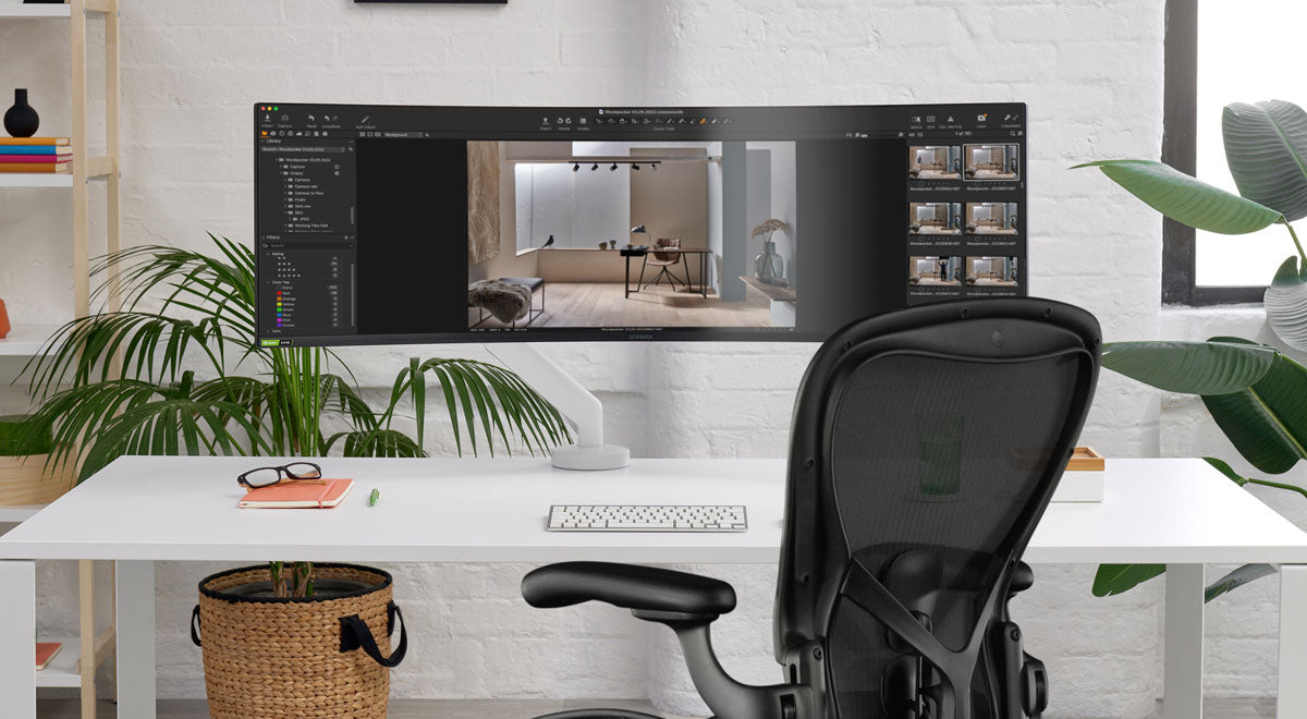 Vue de face d'un bras de moniteur Flo X blanc de CBS fixé à un bureau blanc, placé devant une chaise de bureau Aeron noire de Herman Miller.