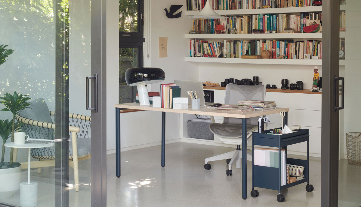Un bureau à domicile lumineux et moderne équipé d'un bureau Herman Miller OE1, d'un chariot de bureau OE1 bleu et d'une chaise ergonomique Cosm.