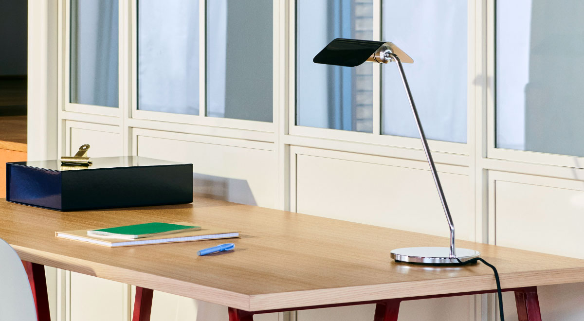 Une lampe de bureau Apex noire et argentée de HAY, placée dans le coin arrière d'un bureau en bois.
