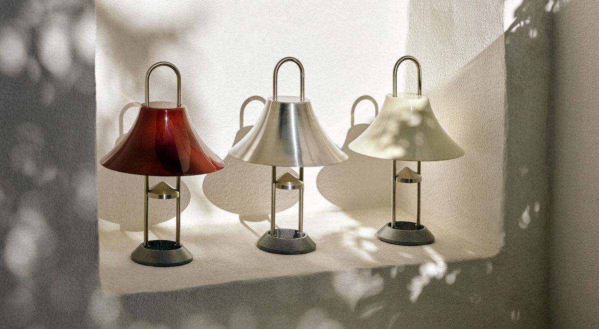 Trois lampes portables HAY Mousqueton rouges, argentées et blanches, disposées dans une niche murale blanche.