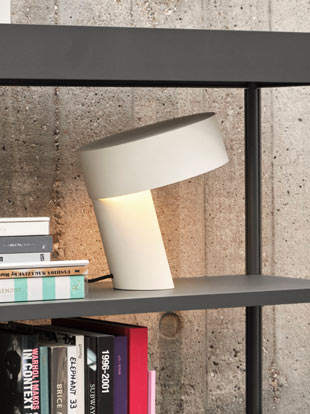 Une lampe Slant blanche de HAY, placée sur une bibliothèque noire dans une maison.
