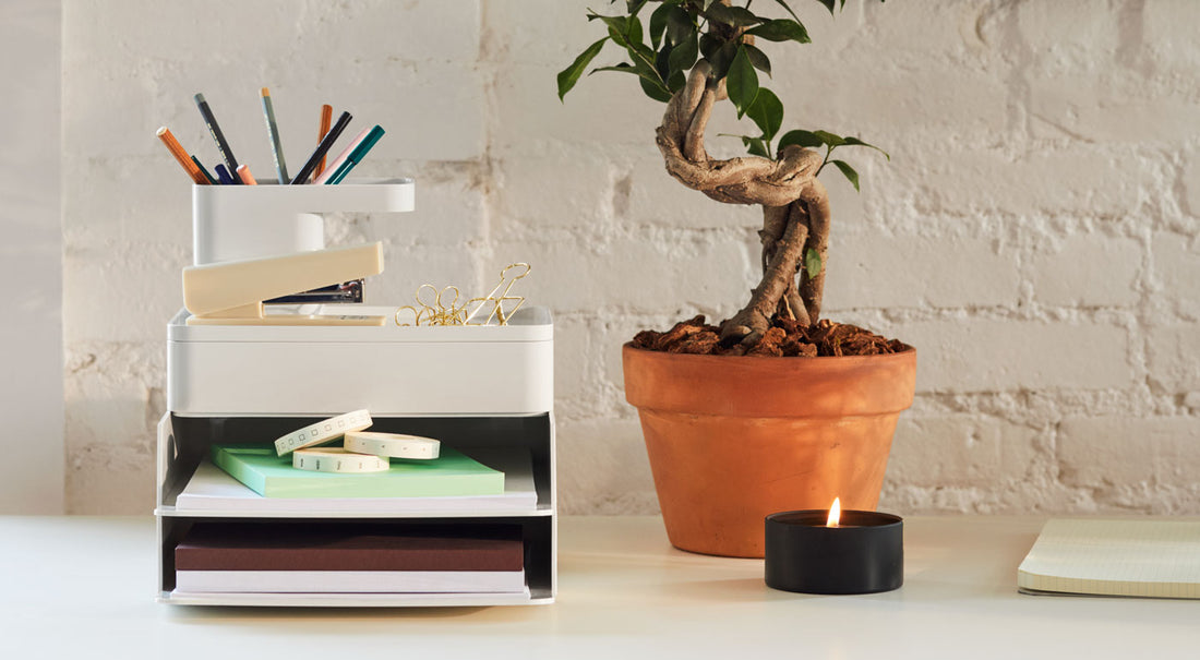 Un ensemble d'accessoires de rangement pour bureau Formwork gris béton, accompagnés d'une plante et d'une bougie sur un bureau.