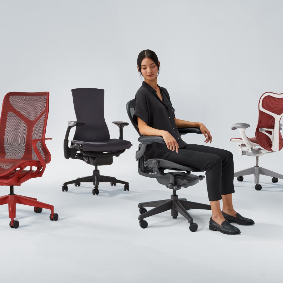 Quatre chaises de bureau Herman Miller, dont une Cosm à dossier moyen rouge canyon, une Embody noire, une Aeron graphite avec une femme assise dessus et enfin une Mirra 2 avec un cadre blanc et une assise et un dossier rouges