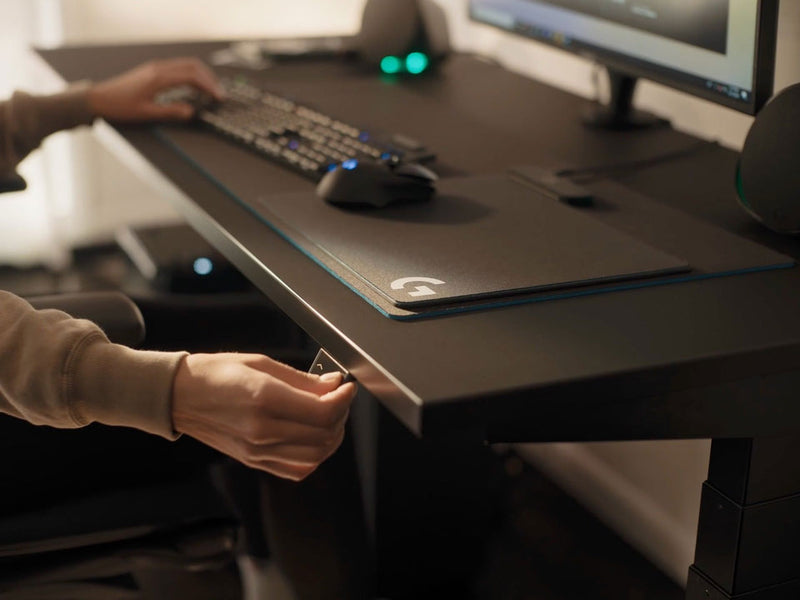 Vidéo d'une personne assise sur un bureau de jeu Nevi noir de Herman Miller, appuyant sur un bouton pour abaisser le bureau.