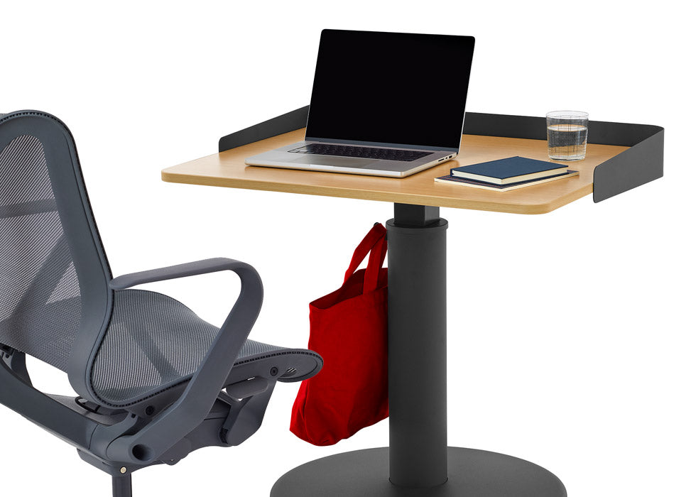 Une chaise de bureau Cosm bleue de Herman Miller, placée devant un bureau debout OE1 noir et gris cendré de Herman Miller, équipé d'un écran enveloppant en option.