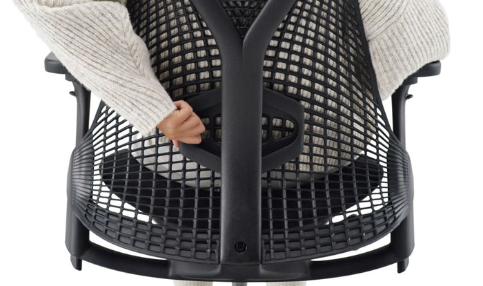 Vue arrière en gros plan d'une personne assise sur une chaise de bureau Sayl noire de Herman Miller, tendant le bras pour déplacer le support lombaire réglable en hauteur.