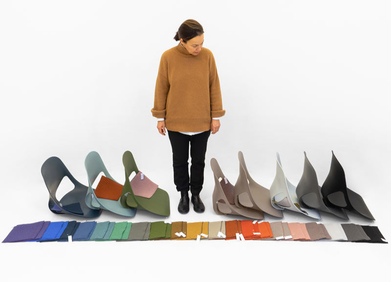 Une femme debout à côté de plusieurs éléments de la chaise de bureau Zeph, avec un éventail de couleurs de tissu étalé devant elle.