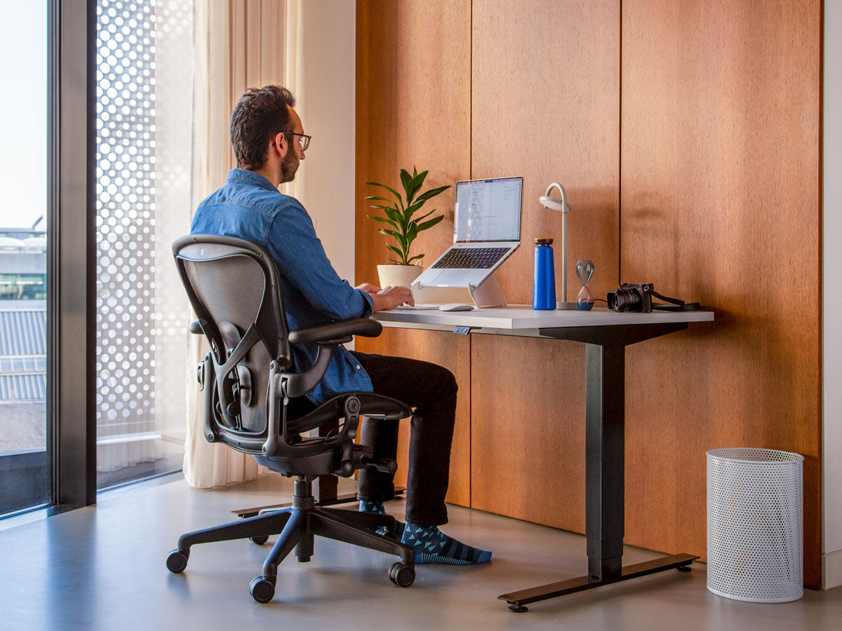 Photo d'un homme assis dans une chaise de bureau Aeron en graphite, montrant correctement que les pieds doivent être posés sur le sol pour être assis correctement.