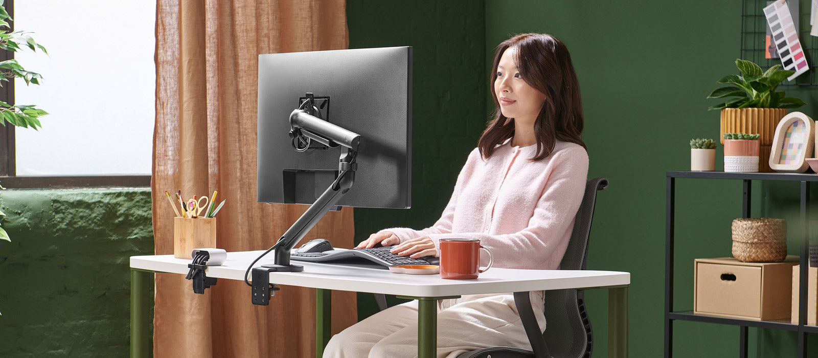 Une femme était assise à un bureau Herman Miller OE1, travaillant devant un écran fixé à un bras de support Flo noir.