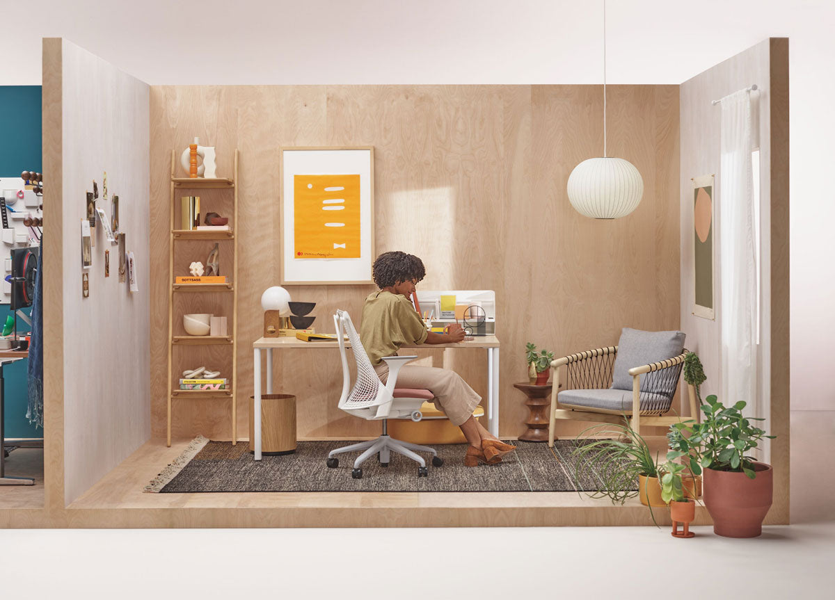 Femme assise à un bureau dans un bureau à domicile neutre, sur une chaise de bureau Sayl blanche devant un bureau OE1 avec des pieds blancs et un plateau en bois clair.