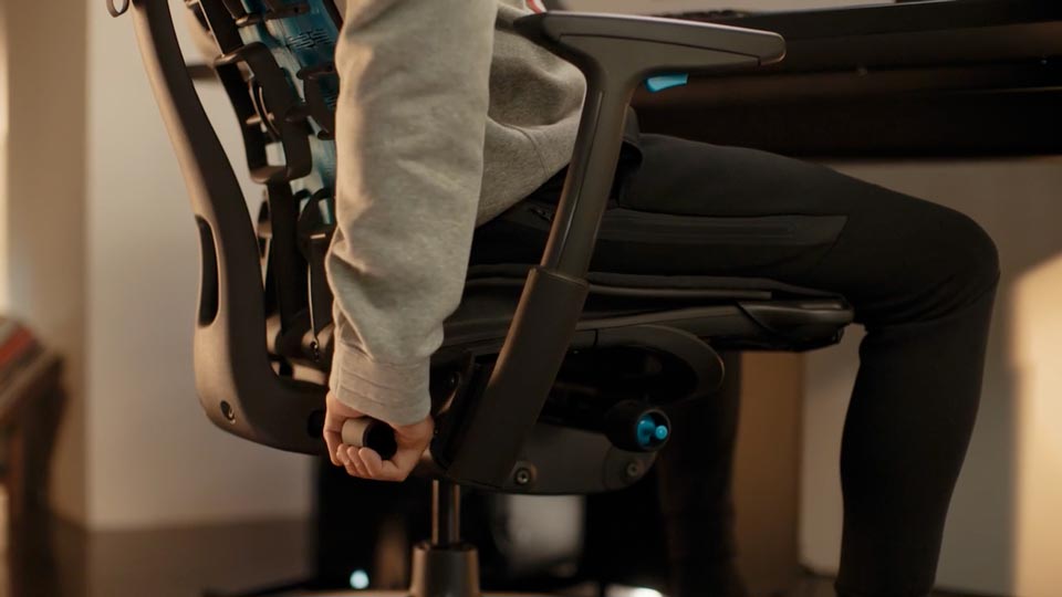 Vidéo d'une personne assise dans un fauteuil de jeu Embody noir et bleu de Herman Miller, tendant la main derrière le fauteuil pour régler le dossier.