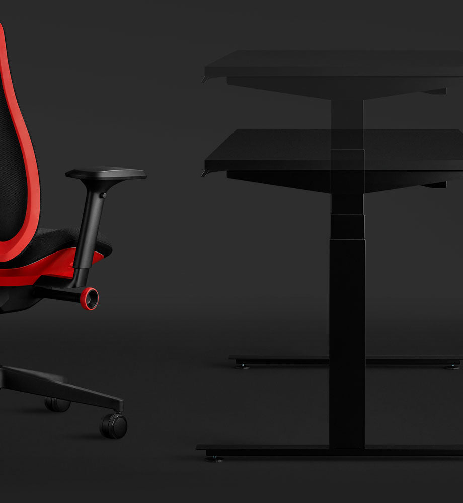 Vue latérale d'un bureau de jeu Nevi noir et d'un fauteuil de jeu Vantum rouge d'Herman Miller, mettant en évidence l'aspect assis-debout du bureau.