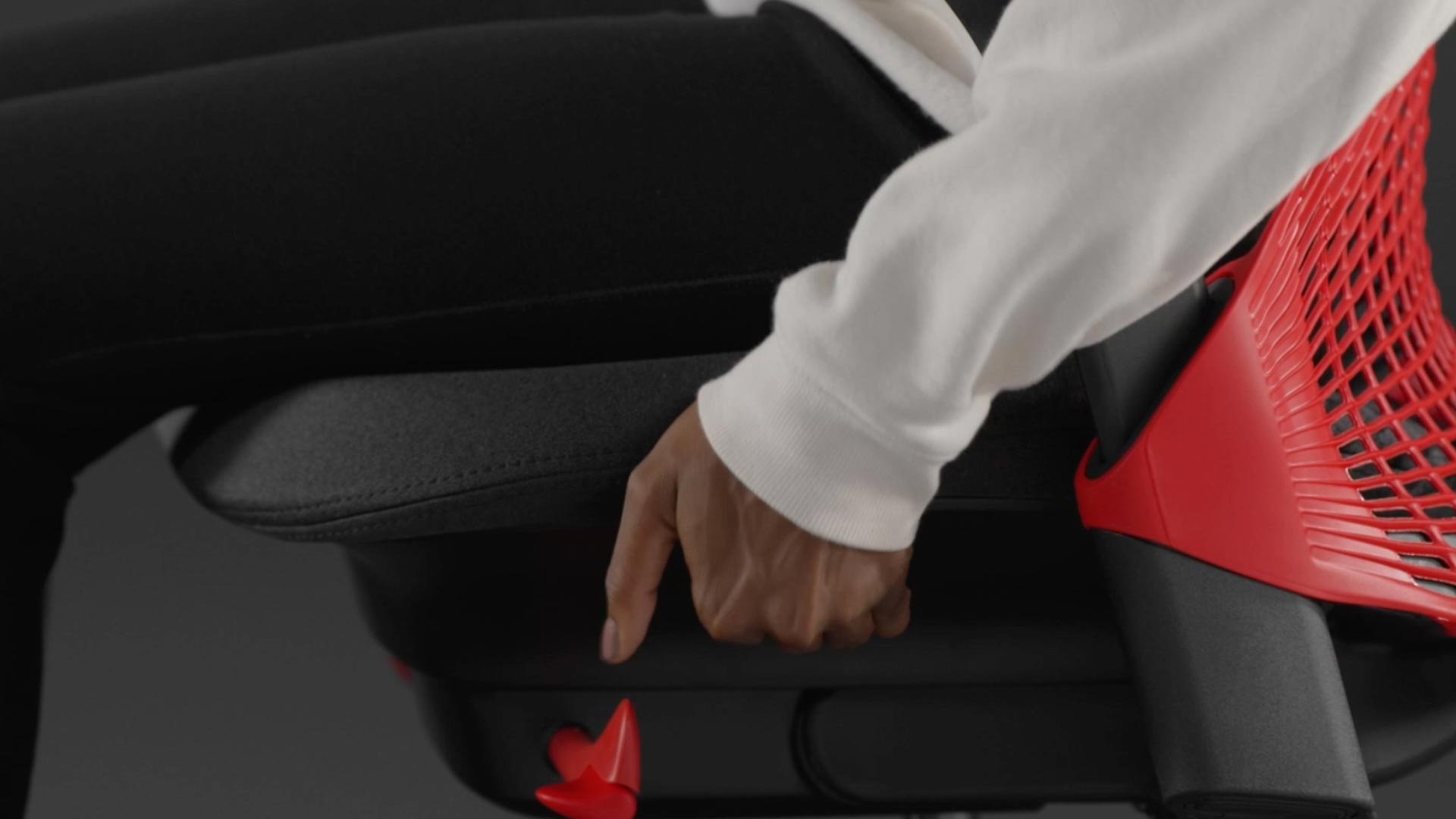 Vidéo d'une personne assise dans un fauteuil de jeu Sayl rouge et noir de Herman Miller, qui tend la main à côté du fauteuil pour régler la profondeur de l'assise.