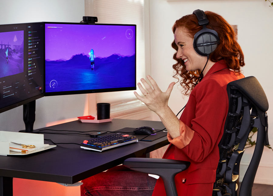 Photo du Dr Lindsey Migliore souriant en jouant à un jeu vidéo dans un fauteuil gaming Embody cyan avec un bureau gaming Nevi noir.