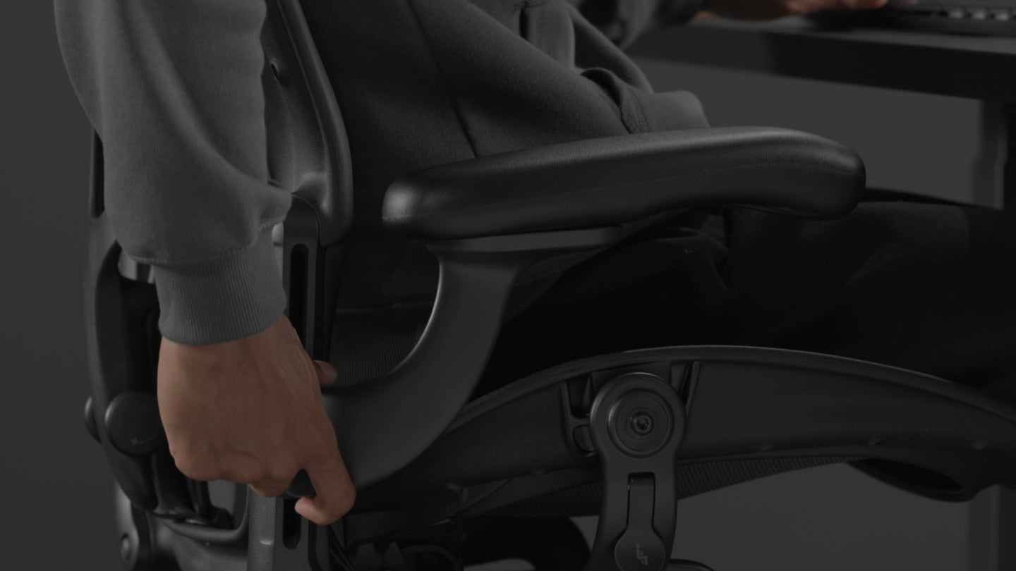 Vidéo d'une personne assise dans un fauteuil de jeu Aeron noir de Herman Miller, tendant la main à côté du fauteuil pour régler les accoudoirs.
