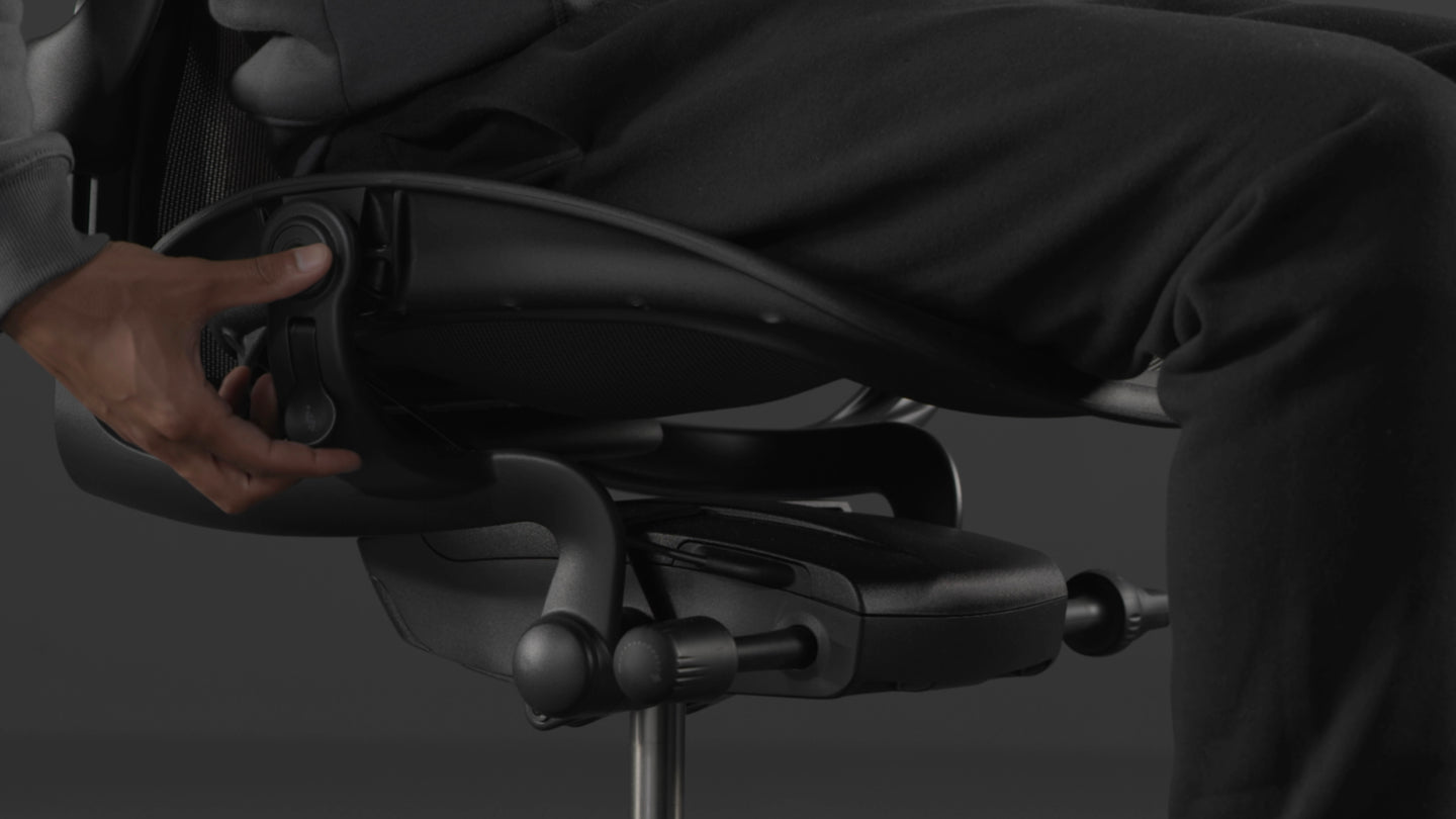 Vidéo d'une personne assise dans un fauteuil de jeu Aeron noir de Herman Miller, tendant la main à côté du fauteuil pour régler la hauteur de l'assise.