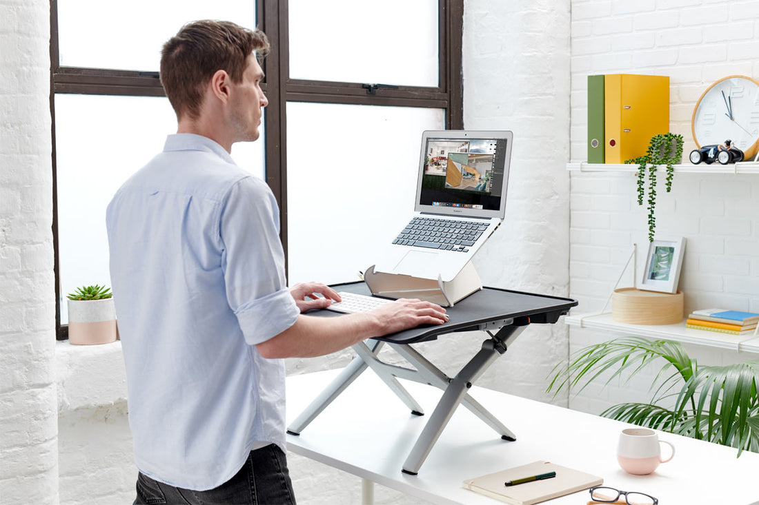 Un employé de bureau utilisant un rehausseur CBS Monto Sit Stand pour travailler debout.