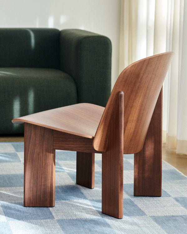 Vue arrière d'un fauteuil lounge Chisel en noyer de HAY, placé dans un espace intérieur sur un tapis à carreaux bleus.