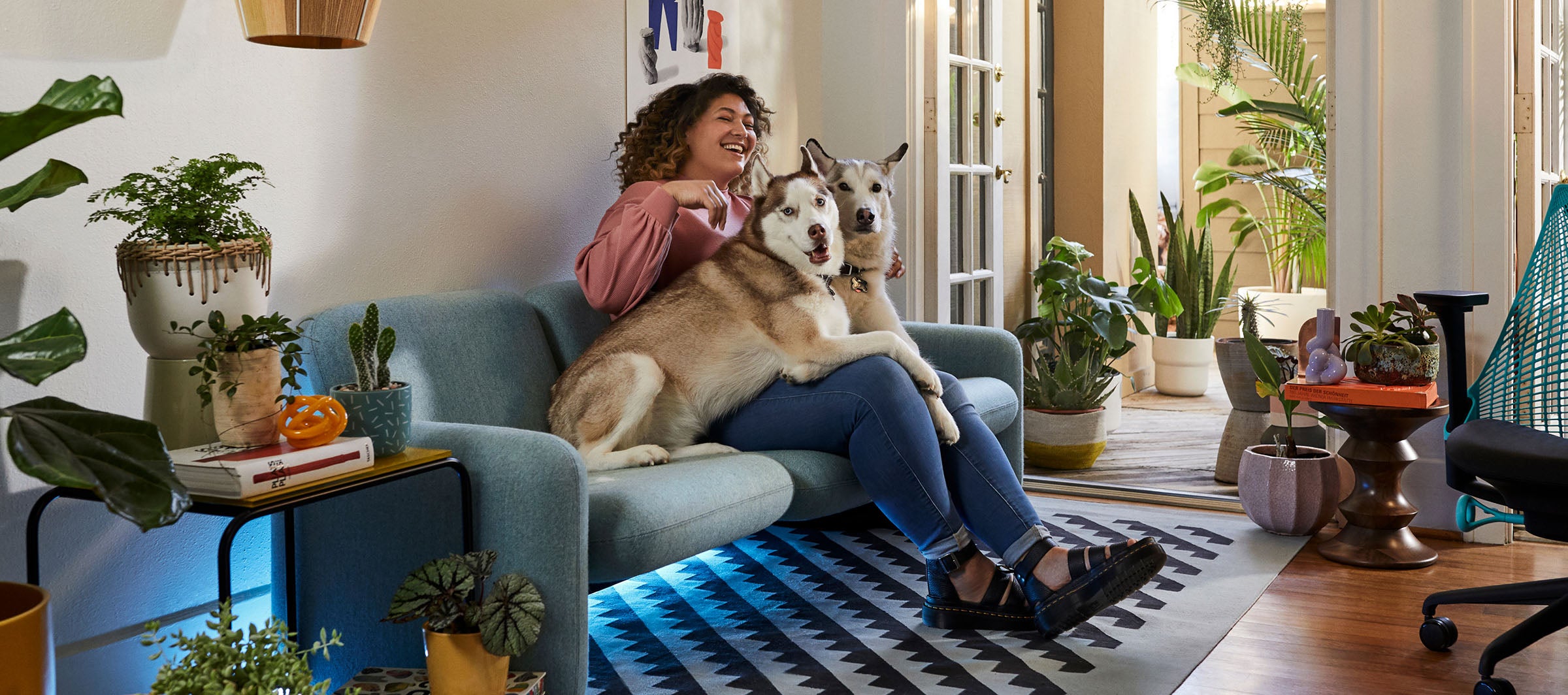 Friskk assis sur le canapé Wilkes en vert avec ses deux chiens, le fauteuil de jeu Sayl en noir et bleu océan à côté