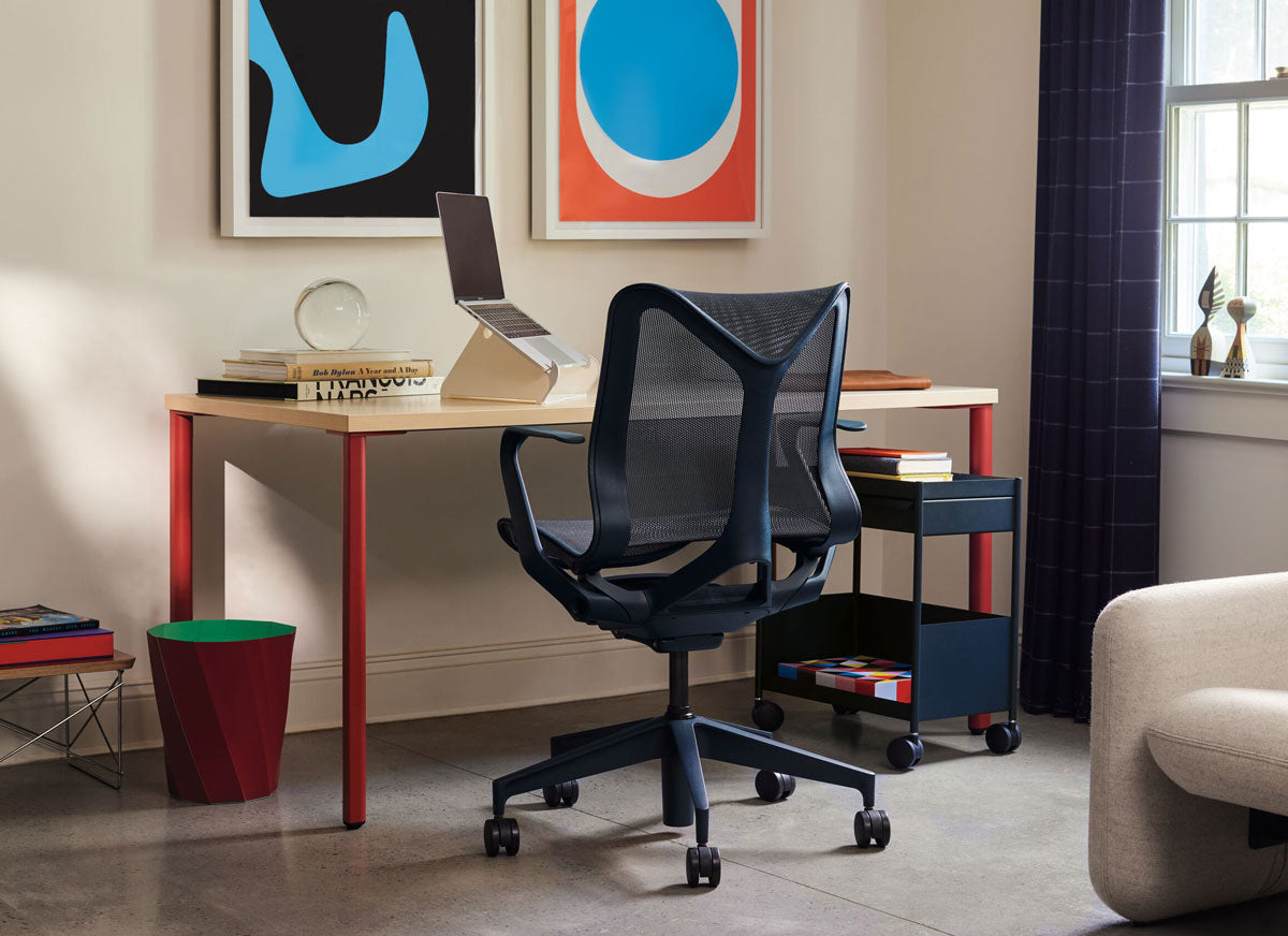 Un bureau à domicile composé d'un bureau OE1 avec plateau en bois et pieds rouges, et d'une chaise de bureau ergonomique Herman Miller Cosm bleu nuit.