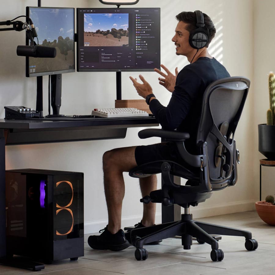 Le joueur et streamer Xaryu dans une configuration gaming, assis sur une chaise gaming Herman Miller Aeron avec un bureau gaming assis-debout Nevi noir et deux écrans sur des bras porte-écrans Ollin