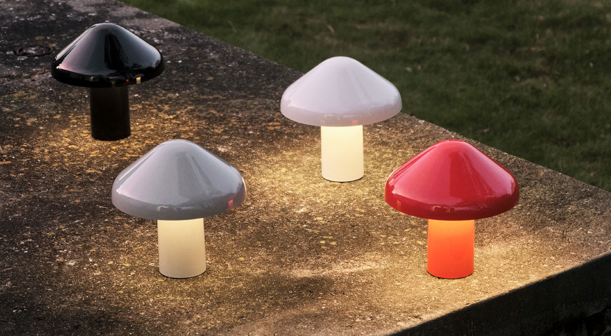 Quatre lampes de table portables Pao de HAY en noir, blanc, gris et rouge. Installées à l'extérieur dans un jardin, elles diffusent une douce lumière chaleureuse.