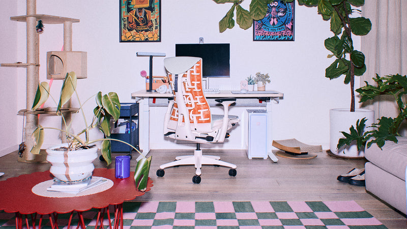 Un fauteuil gaming Herman Miller Embody blanc et orange, avec un revêtement gris, dans un salon bien éclairé aménagé pour le jeu sur PC.