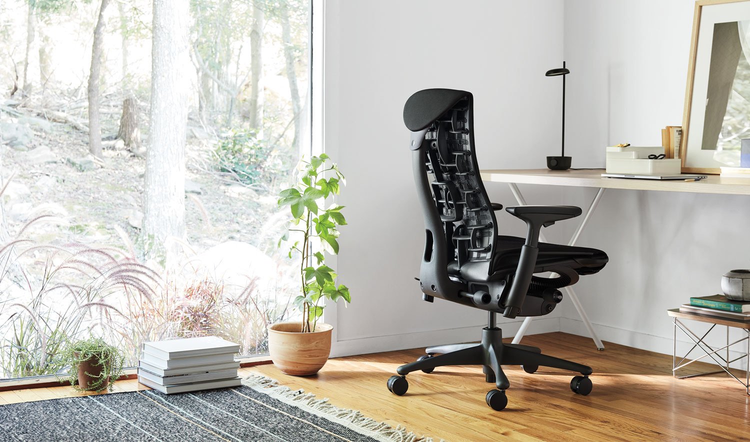 Un siège de bureau Embody noir de Herman Miller, situé dans un environnement intérieur. L'espace comprend des éléments tels que le mobilier, le sol et des éléments décoratifs comme un pot de fleurs et un vase.