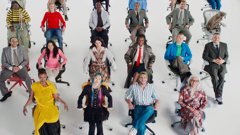 Un groupe important et diversifié de personnes assises sur une sélection de chaises de bureau ergonomiques Herman Miller dans un studio blanc.