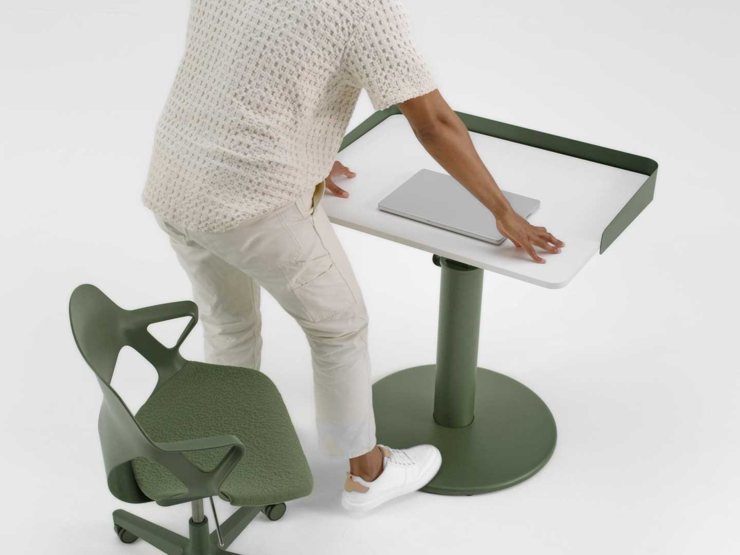 Vidéo montrant un homme debout sur une chaise Zeph verte de Herman Miller, qui relève à l'aide de son pied un bureau debout OE1 vert et blanc de Herman Miller.