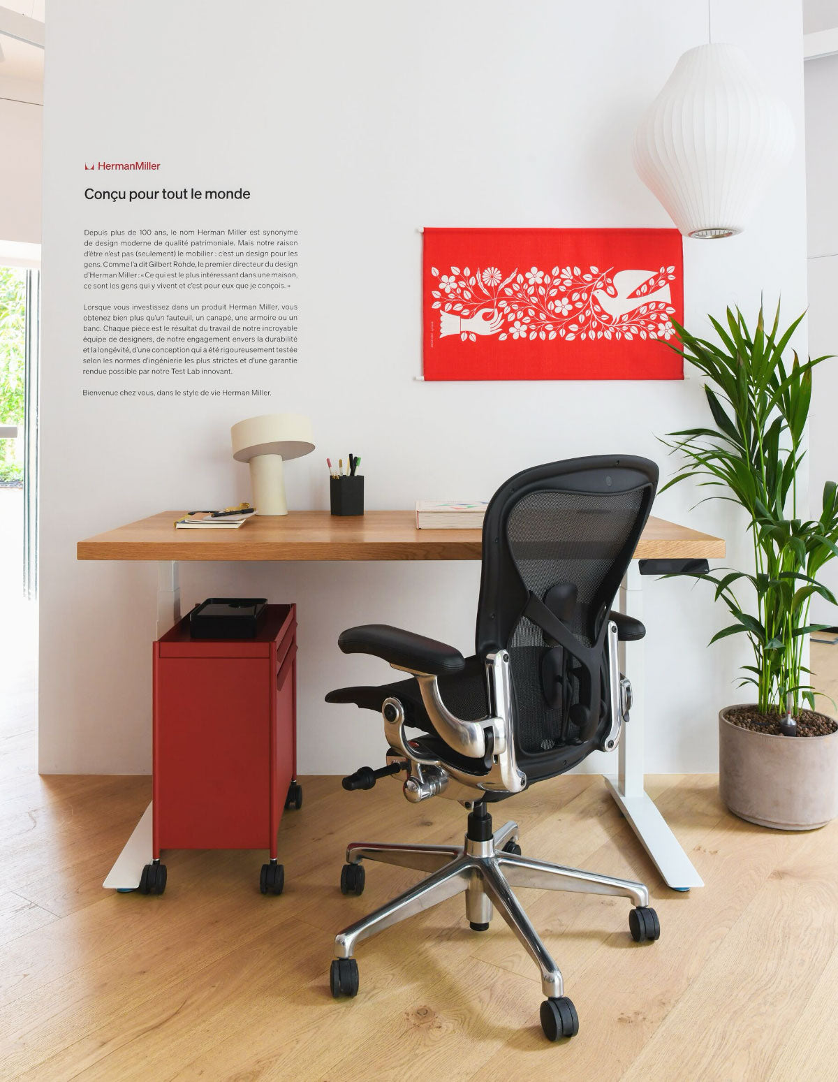 Une chaise Aeron Herman Miller noire et chromée dans un bureau à domicile équipé d'un bureau Jarvis en chêne, d'une lampe Slant blanche et d'un chariot de rangement OE1 rouge dans notre showroom de Paris.