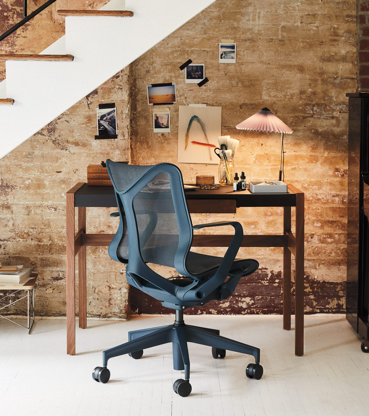 Espace de bureau à domicile sous un escalier avec un siège Cosm à dossier bas bleu nuit devant un bureau en bois avec une lampe de bureau Hay Matin