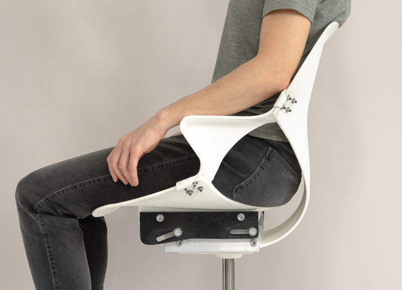 Vue latérale d'une personne assise sur une chaise de bureau Zeph à l'état brut, montrant la flexibilité du dossier