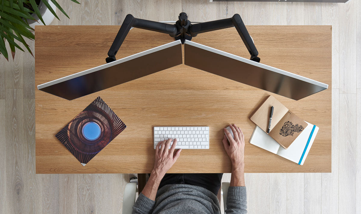 Vue de dessus d'un bureau en bois équipé d'un double bras de support Lima supportant deux écrans.