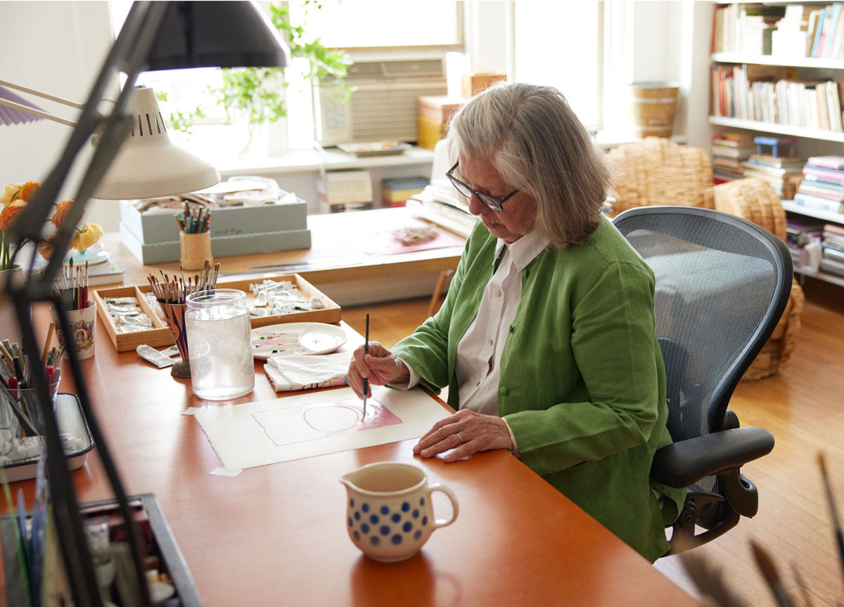 L'artiste Maira Kalman travaille sur une peinture dans un espace studio lumineux depuis son Aeron Herman Miller Onyx.