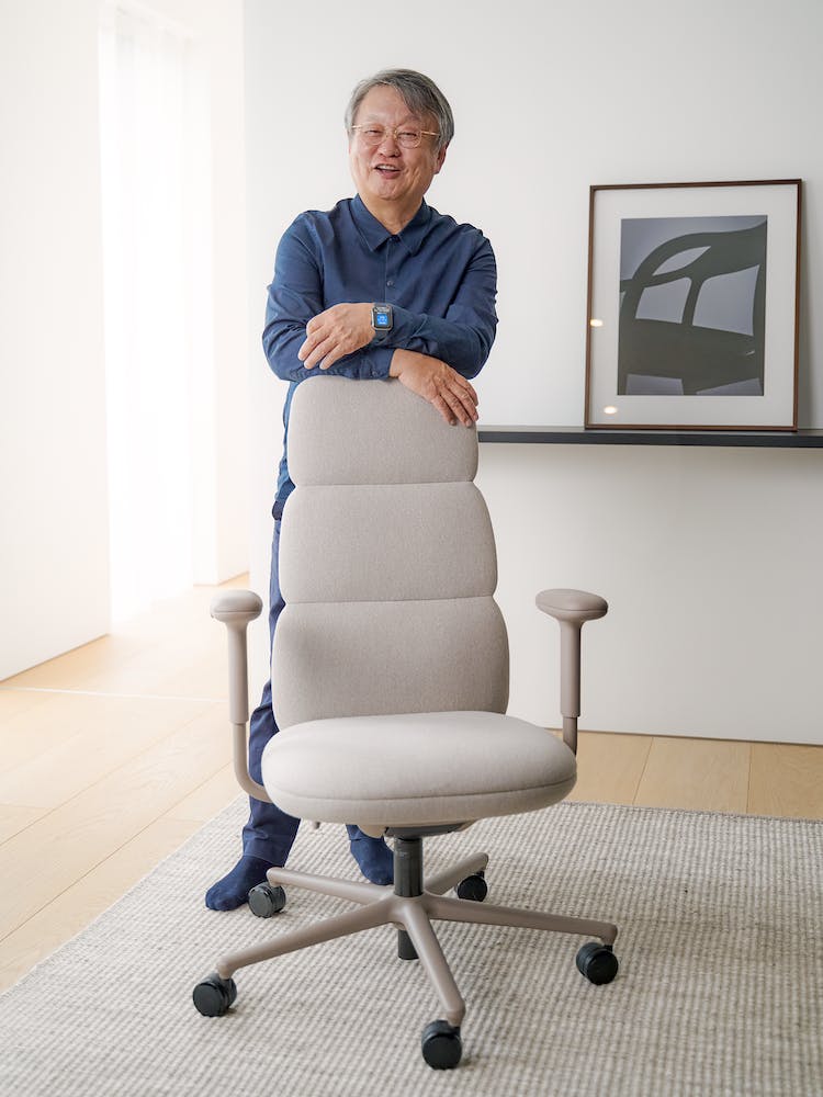 Le designer, Naoto Fukasawa, s'appuyant sur une chaise de bureau Herman Miller Asari. Le décor est constitué d'un sol et d'un mur épurés en arrière-plan.