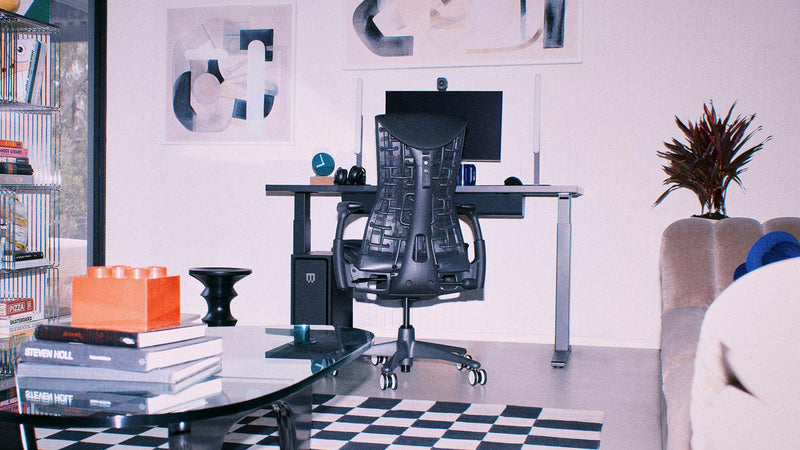 Une chaise de jeu ergonomique Herman Miller Embody noire faisant partie d'un ensemble de jeu sur PC comprenant un bureau assis-debout Nevi dans un espace de vie lumineux.