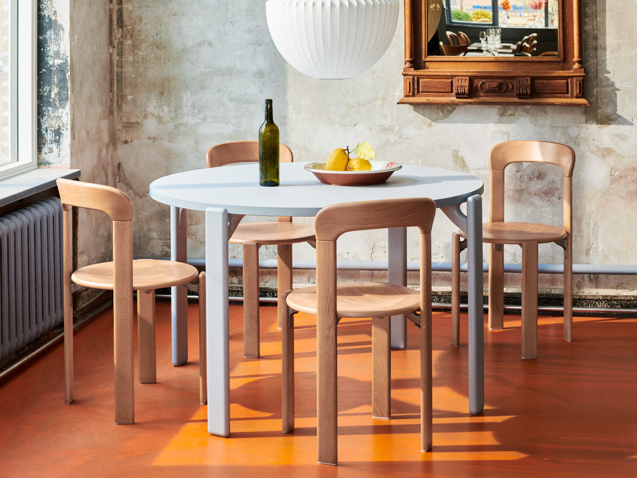 Quatre chaises Rey en hêtre de HAY, disposées autour d'une table à manger Rey bleu ardoise. Dans un cadre domestique, avec une suspension Nelson au-dessus de la table et une corbeille de fruits et une bouteille de vin sur le plateau.