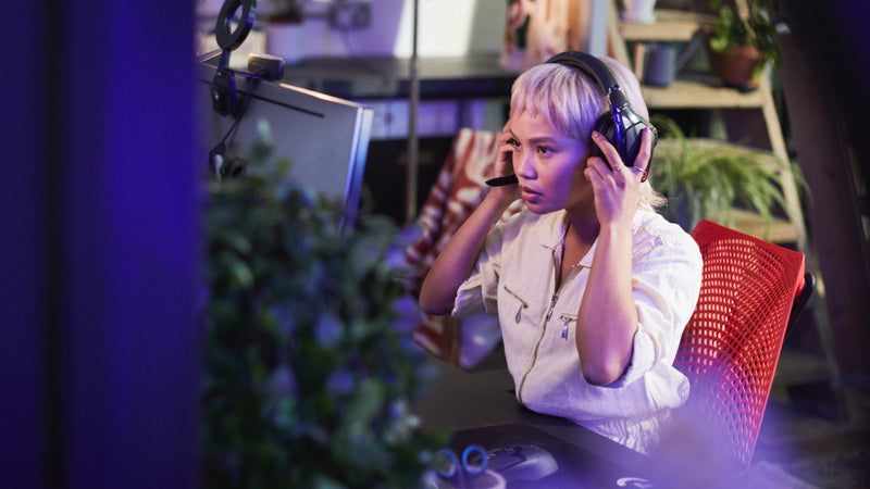 Vidéo d'une femme assise dans un fauteuil de jeu Sayl rouge et noir de Herman Miller, mettant des écouteurs et jouant à un jeu vidéo.