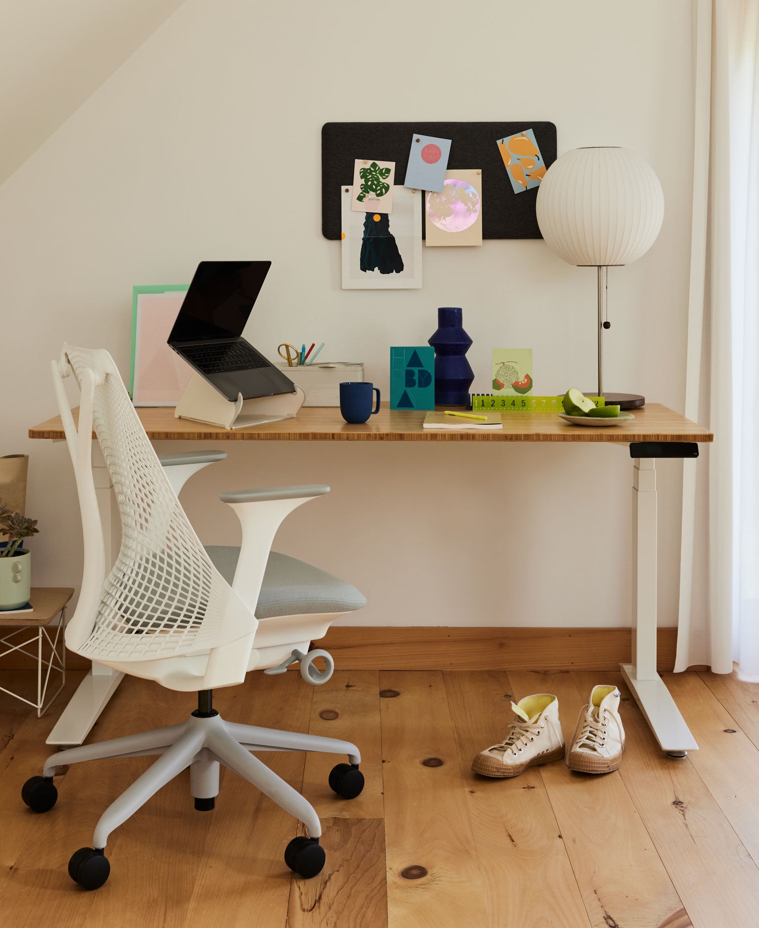 Bureau à domicile avec chaise de bureau Sayl avec structure blanche et coussin d'assise gris pâle devant un bureau assis-debout Jarbis avec structure blanche et plateau en bois massif, avec un ordinateur portable sur un support Oripura et une lampe de table Nelson Bubble
