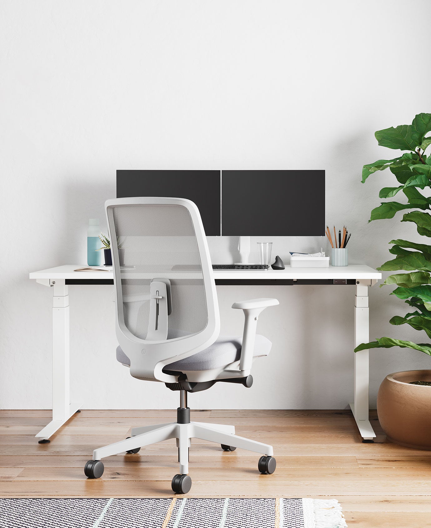 Bureau à domicile avec chaise de bureau Verus en blanc minéral avec coussin d'assise gris pâle, devant un bureau assis-debout Nevi en blanc avec deux écrans sur des bras porte-moniteurs