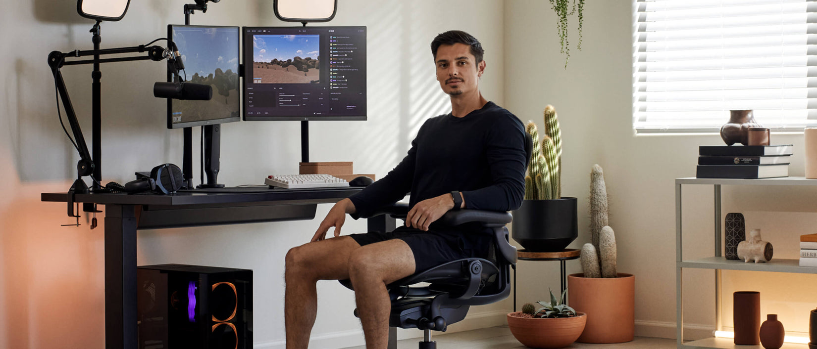 Photo du joueur Xaryu assis face à la caméra dans un fauteuil de jeu Aeron graphite, avec son installation de jeu derrière lui, composée d'un bureau de jeu Nevi et de deux bras pour double écran Ollin.