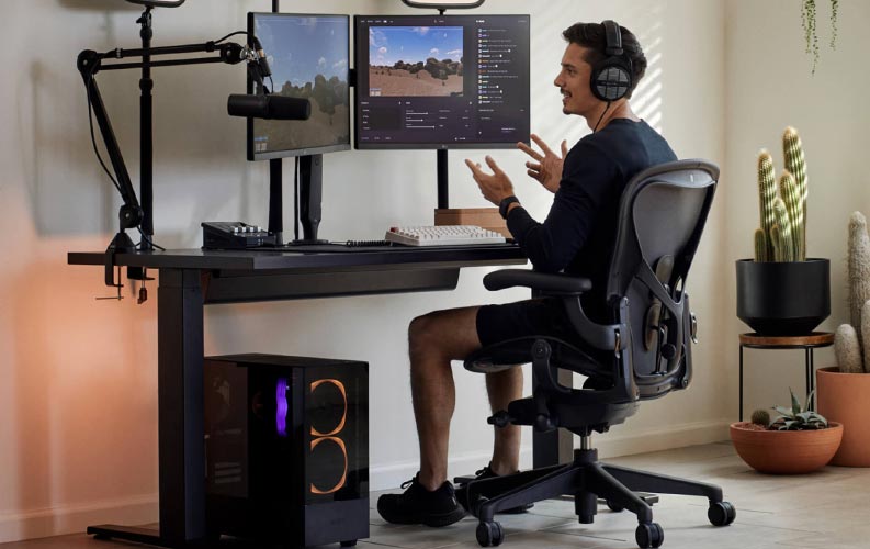 Le joueur et streamer Xaryu dans une installation de jeu, assis sur une chaise de jeu Herman Miller Aeron avec un bureau de jeu assis-debout Nevi noir et deux écrans sur des bras pour moniteur Ollin